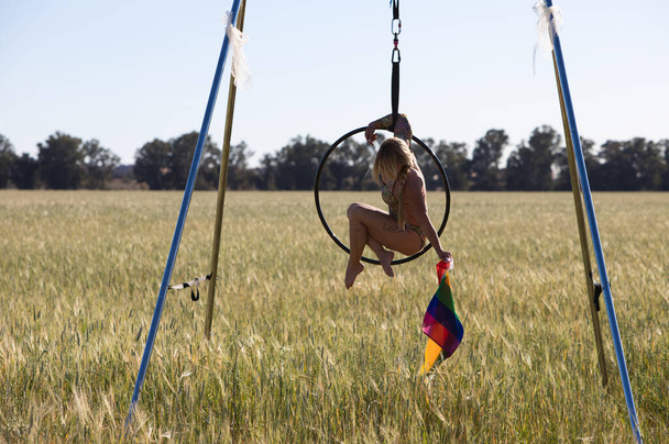 young and beautiful blonde woman doing aerobic exercises on a hoop, in her hand the gay pride flag claiming the rights of gays and lesbians. Concept of gay pride - Photo, Image