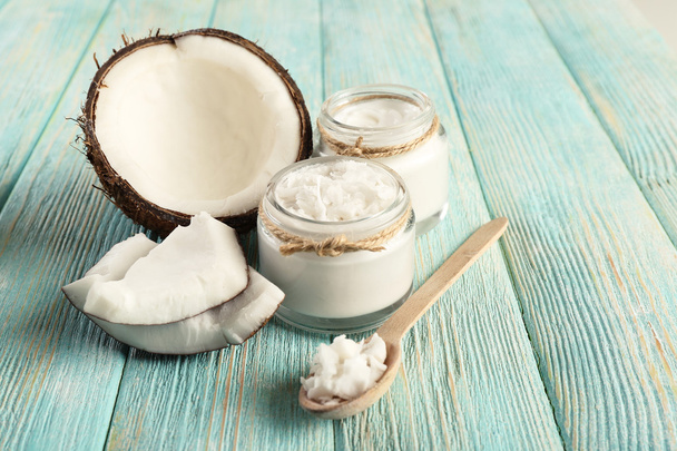 Fresh coconut oil in glassware and wooden spoon on color wooden table background - Valokuva, kuva