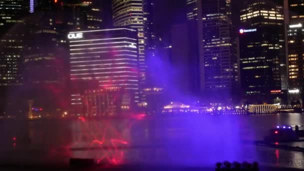 Mayıs 1, 2023. İşletme Bölgesi gökdelenlerinin arka planına sahip Marina Bay Sands 'in önündeki gezinti alanı boyunca ışık ve su ile dans eden fıskiyelerin gösterimi. - Video, Çekim