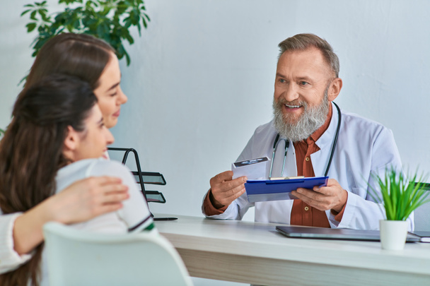 веселий сірий бородатий лікар розмовляє, обіймаючи пару lgbt, яка щиро посміхається, IVf концепція - Фото, зображення