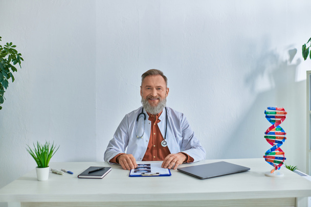 веселий гінеколог сидить за своїм столом в офісі і посміхається ультразвуком дитини - Фото, зображення