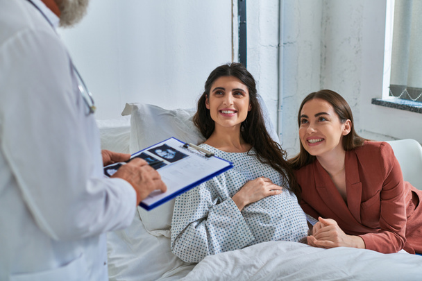 alegre pareja lesbiana sonriendo al médico sosteniendo ultrasonido del bebé, concepto de fertilización in vitro - Foto, Imagen
