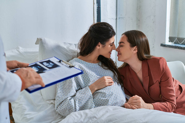 feliz pareja lesbiana frotando narices en la cita, médico sosteniendo ultrasonido en las manos, concepto ivf - Foto, Imagen