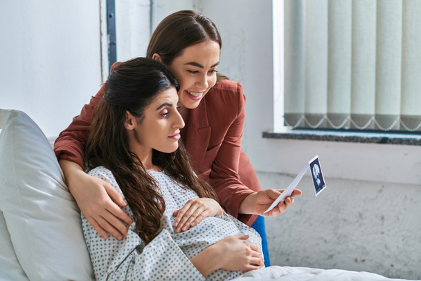 joven pareja lesbiana mirando el ultrasonido de su bebé con las manos en el vientre embarazada, concepto ivf - Foto, imagen