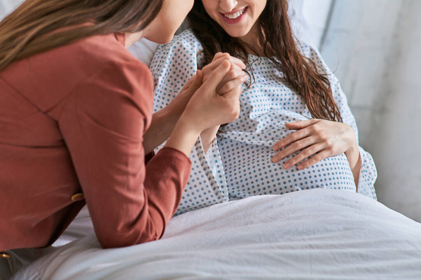 cropped view of smiling lesbian couple holding hands with one hand on pregnant belly, ivf concept - Photo, Image