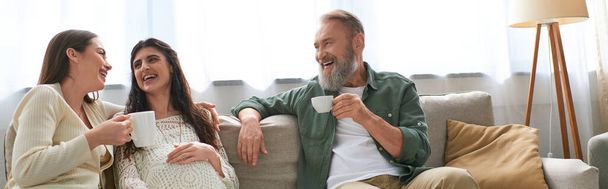 lgbt pareja y padre de uno de ellos sentado en sofá riendo y bebiendo té, concepto ivf, bandera - Foto, Imagen