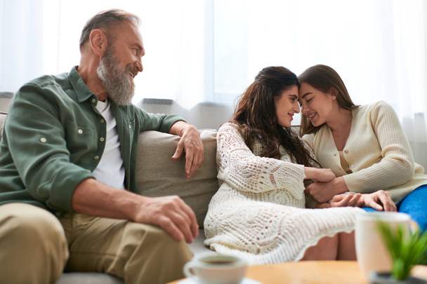 Vater sitzt auf Sofa und schaut liebevoll zu seiner schwangeren Tochter und ihrem Partner, ivf concept - Foto, Bild