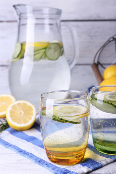 Fresh water with lemon and cucumber in glassware on wooden background - 写真・画像