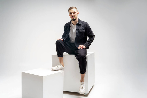 Young handsome guy in a black caton jacket, black pants and a white t-shirt on a gray studio background - Foto, Imagem