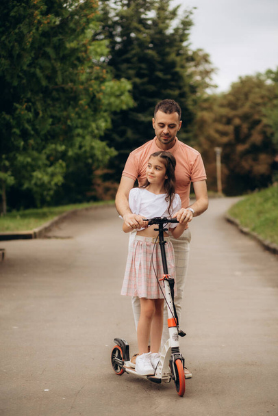 Тато з дочкою в парку вчить їздити на скутері. Високоякісна фотографія
 - Фото, зображення