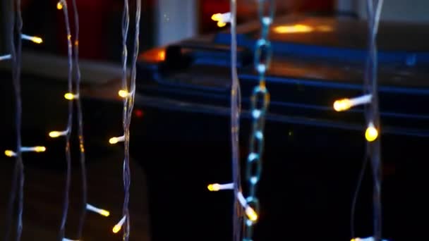 Kerstverlichting. Nieuwjaarsbloemenslinger tegen de achtergrond van een brandend huisraam. Mooie kerstachtergrond. Wazige kleur heldere slinger op het display venster. Kleurrijke Nieuwjaarsachtergrond - Video