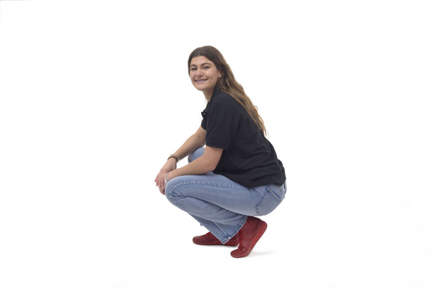side view of a young girl long-haired sitting on her haunches looking at camera on white background - Photo, Image