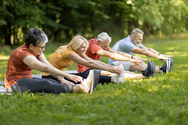 Estilo de vida activo. Grupo de personas mayores deportistas que hacen ejercicio juntos al aire libre, hombres maduros felices y mujeres que se estiran en el césped en el parque, haciendo ejercicio físico afuera, disfrutando del ocio de jubilación - Foto, imagen