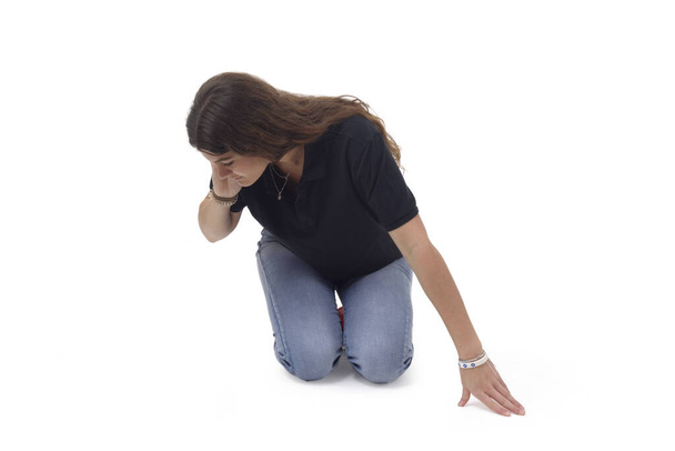una chica que está de rodillas en el suelo buscando algo a un lado sobre un fondo blanco - Foto, imagen