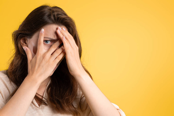 Scared young caucasian lady covers her face with hands, afraid, isolated on yellow studio background, close up. Reaction on stress, horror, bad news, ad and offer, human emotions - Photo, Image