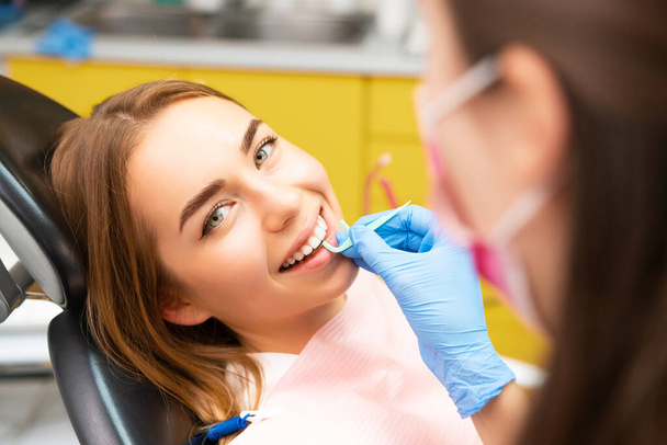 Un dentista instruye a una mujer joven sobre la técnica correcta para usar hilo dental - Foto, Imagen