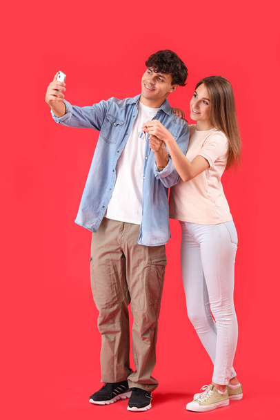 Young couple with key from house taking selfie on red background - Photo, Image