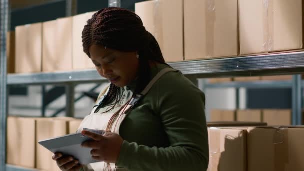 アフリカ系アメリカ人の倉庫ディレクターの肖像画は,小包の配達を監督するためにタブレットを使用して,顧客に送信する準備ができているフルフィルメントセンターの倉庫商品の追跡 - 映像、動画