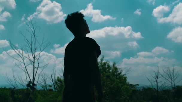 силуэт азиата задумчивого и мыслящего на фоне полных облаков и голубого неба в течение дня - Кадры, видео