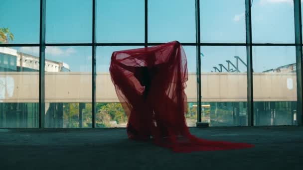 een Aziatische man dansen met een rode doek bedekken zijn lichaam in de voorkant van een gebouw venster gedurende de dag - Video