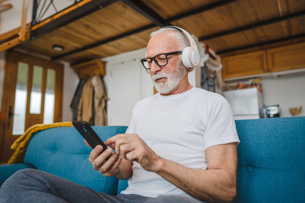 un uomo anziano con le cuffie usa smsrtphone per riprodurre musica a casa - Foto, immagini