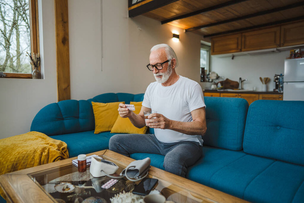 Jeden starszy mężczyzna kaukaski mężczyzna dziadek siedzieć w domu trzymać blister tabletki przeciwbólowe lub witaminy suplement czytać etykieta gotowa do podjęcia leku prawdziwa osoba kopia przestrzeń - Zdjęcie, obraz