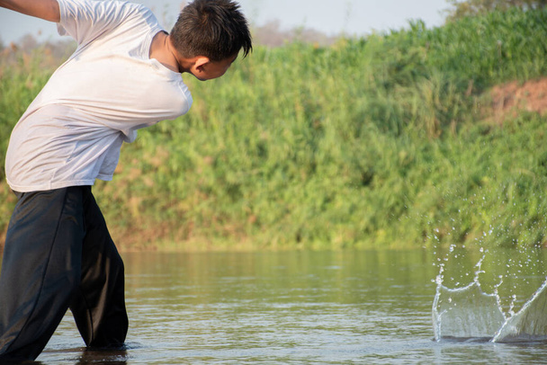 Азіатський хлопчик кидає камінь над поверхнею місцевої річки у вільний час після школи, в русі, концепції для дитячого хобі та дитинства по всьому світу. - Фото, зображення