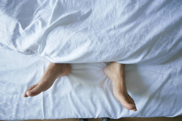 νεαρή γυναίκα ξαπλωμένη με γυμνά πόδια στο κρεβάτι - Φωτογραφία, εικόνα