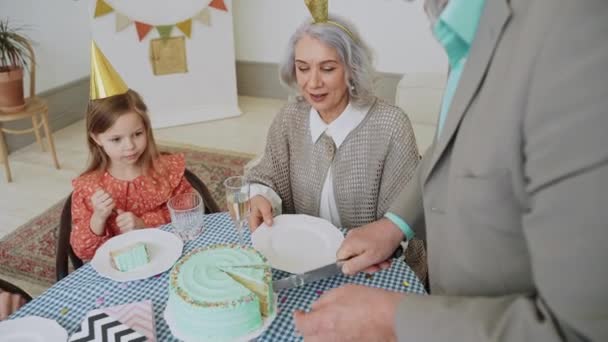 Ein älterer Mann schneidet beim Mädchengeburtstagsessen für die ganze Familie einen Kuchen an. Glückliche Familie bei der Feier. Die Großeltern verbringen Zeit mit der Enkelin. Pastellfarbene Party. Hochwertiges 4k Filmmaterial - Filmmaterial, Video