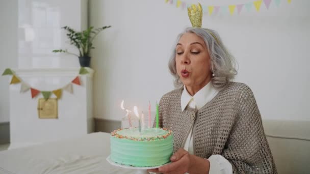 Une femme âgée souffle une bougie sur un gâteau à son dîner d'anniversaire et regarde sa famille. Soirée pastel. Bonne grand-mère moderne. Images 4k de haute qualité - Séquence, vidéo