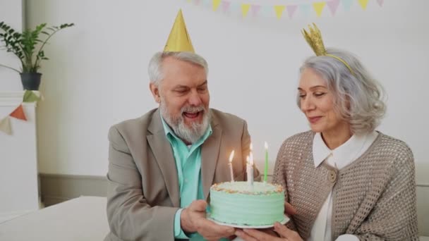 Пожилая пара задувает свечу на торте на праздничном ужине. Пастельная цветная вечеринка. Счастливые бабушка и дедушка. Высококачественные 4k кадры - Кадры, видео