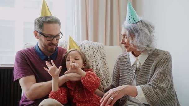若い女の子は誕生日パーティーで父親と祖母と楽しく抱き合っています。祖母と孫娘がキスしてる。家族の集まりだ。高品質4k映像 - 映像、動画