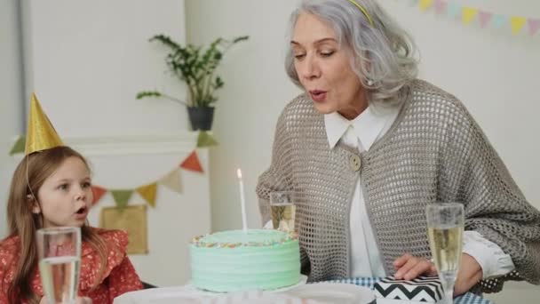 Una donna anziana soffia una candela su una torta alla sua cena di compleanno. La famiglia abbraccia e si congratula con la nonna per il suo compleanno. Festa color pastello. Buona nonna. Filmati 4k di alta qualità - Filmati, video