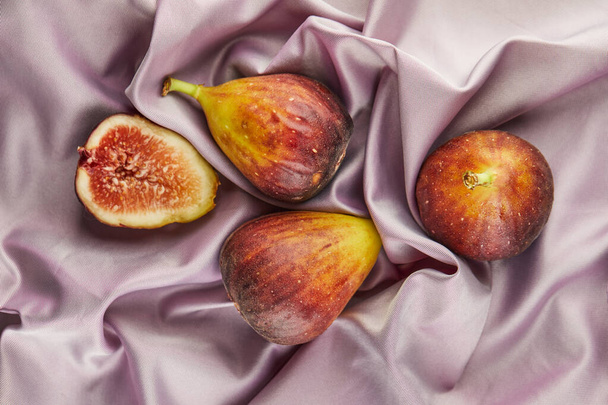 Whole fig and half lie on purple silk. - Photo, Image