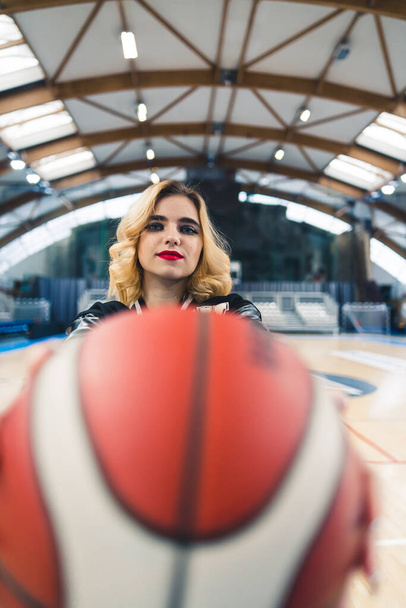 Mulher caucasiana jovem mostrando um basquete para a câmera em uma quadra interna. Foto de alta qualidade - Foto, Imagem