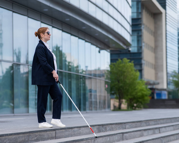 Mujer de negocios ciega descendiendo escaleras con un bastón táctil de un centro de negocios - Foto, Imagen