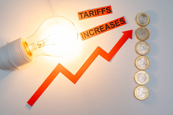 Osvětlená žárovka, vedle mincí a vzestupné čáry, a text Zvýšení tarifů. Zvýšení nákladů na energii. - Fotografie, Obrázek