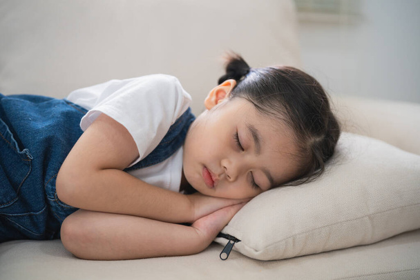 Cute little girl child sleeping on couch sofa with soft pillows at living room at home. Baby girl lying on the sofa couch bed. - Photo, Image