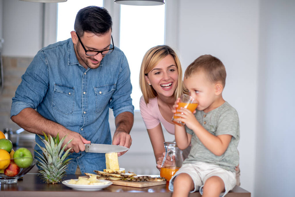 Молоді батьки розважаються зі своїм сином на кухні вдома, готуючи фруктові салати
. - Фото, зображення