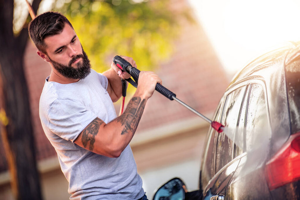 若い魅力的な男は洗車で彼の車を屋外で掃除します.洗濯,ビジネス,ライフスタイルと人々の概念. - 写真・画像