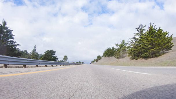 An einem klaren Wintertag fährt ein Auto auf dem ikonischen Highway 101 in der Nähe von San Luis Obispo, Kalifornien. Die umliegende Landschaft ist bräunlich und gedämpft, mit sanften Hügeln und Küstenabschnitten - Foto, Bild