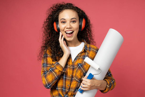 An attractive, young girl in construction headphones and with a roller and paper in her hands - Photo, Image