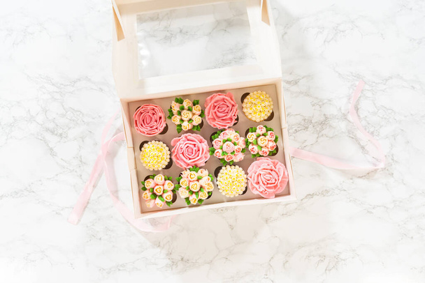 Enveloppé dans une boîte à cupcake en papier blanc immaculé, chaque cupcake gourmet est une œuvre d'art, ornée de fleurs de glaçage à la crème au beurre magnifiquement conçues pour ressembler à des roses et des tulipes vibrantes.. - Photo, image