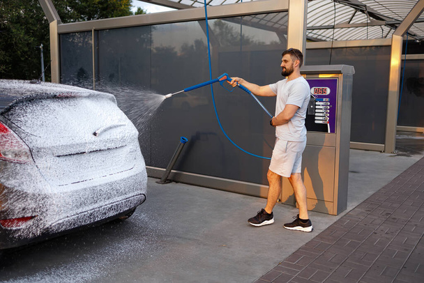 Un homme applique de la mousse détergente à la surface d'une voiture. Une voiture dans un lave-auto libre-service. - Photo, image