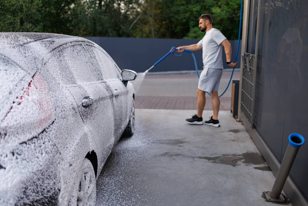 Le côté de la voiture est recouvert de mousse, la personne en arrière-plan applique de la mousse sur la voiture. Une voiture dans un lave-auto libre-service. - Photo, image