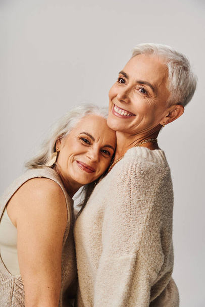 happy mature lady leaning on chest of lifelong female friend on grey, positive and stylish aging - Photo, Image