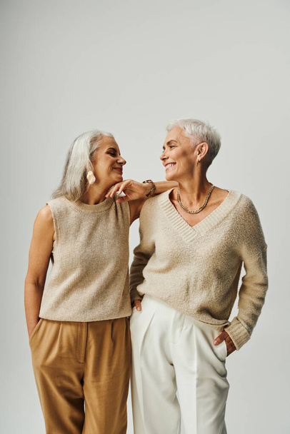 trendy senior women in pastel clothes looking at each other on grey, fashionable long-life friends - Photo, Image