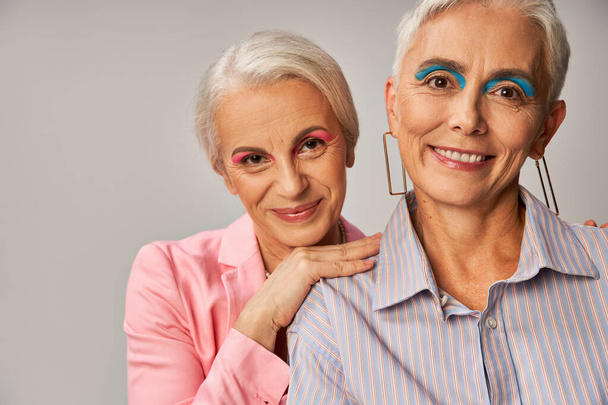 Porträt modischer Seniorinnen mit silbernem Haar und Make-up, die in die Kamera lächeln auf grau - Foto, Bild