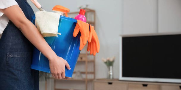Ένα καθαρισμό γυναίκα στέκεται μέσα σε ένα κτίριο που κατέχουν έναν μπλε κάδο που πληρούνται με χημικά και τις εγκαταστάσεις για νοικοκύρεμα στο χέρι.. - Φωτογραφία, εικόνα