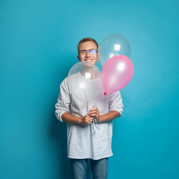 Renkli mavi stüdyo arka planında duran balonları tutan mutlu yakışıklı adam. - Fotoğraf, Görsel